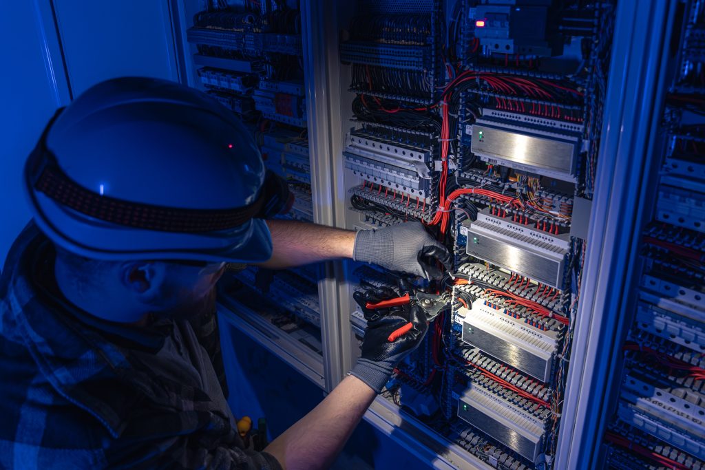 male electrician works switchboard overalls against backdrop emergency lighting